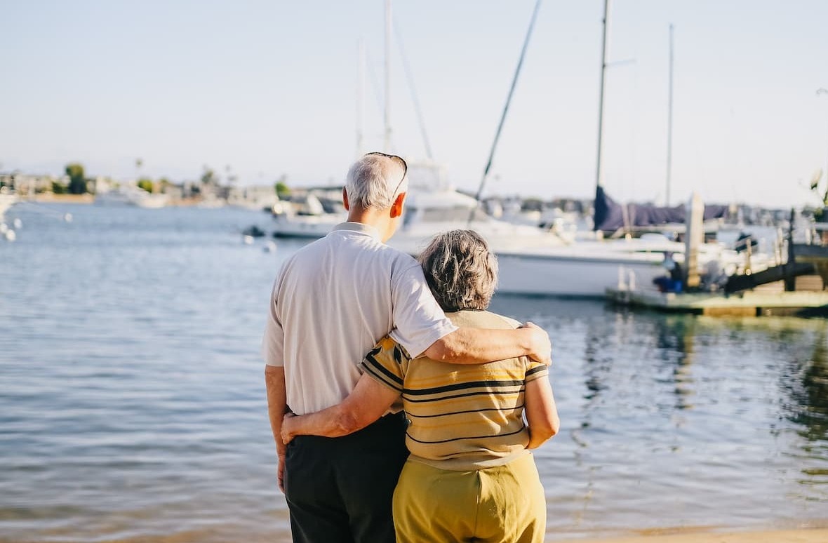 elderly couple looking out from beach to boats. 