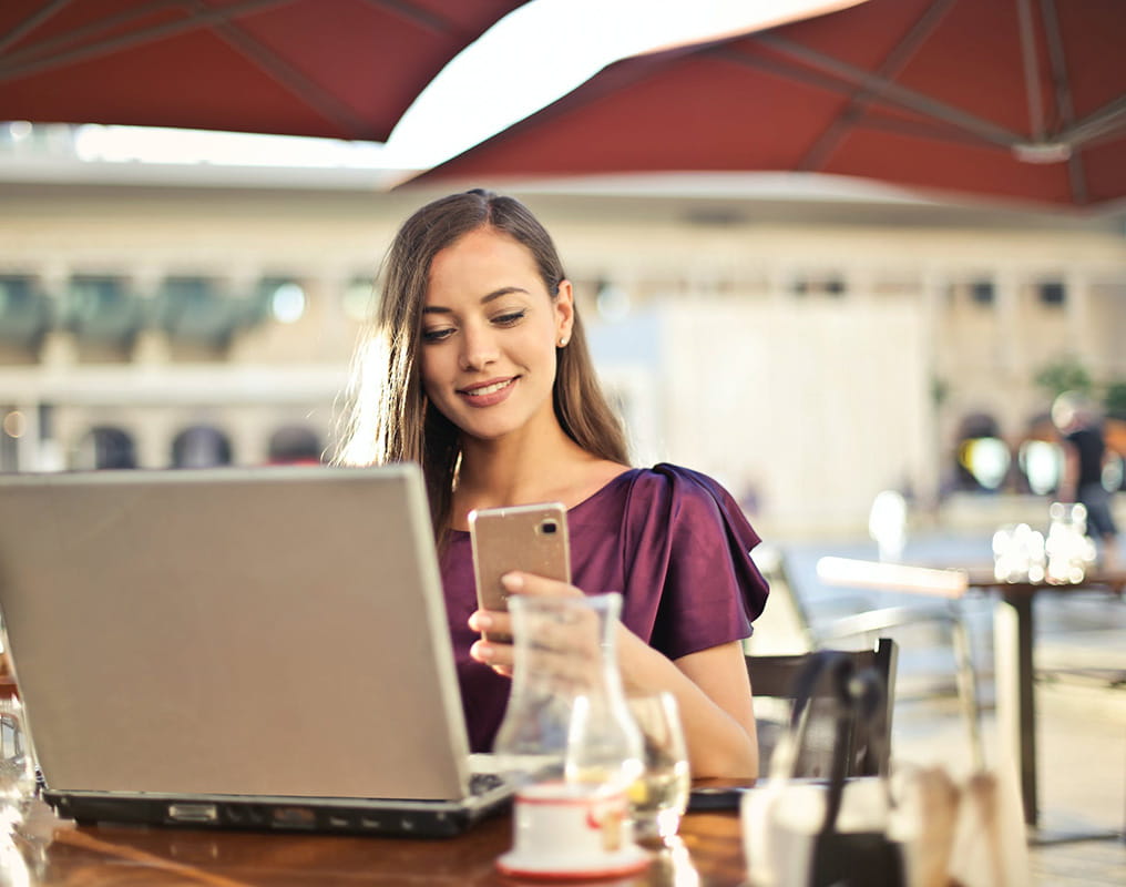 Young woman using phone and laptop in cafe.