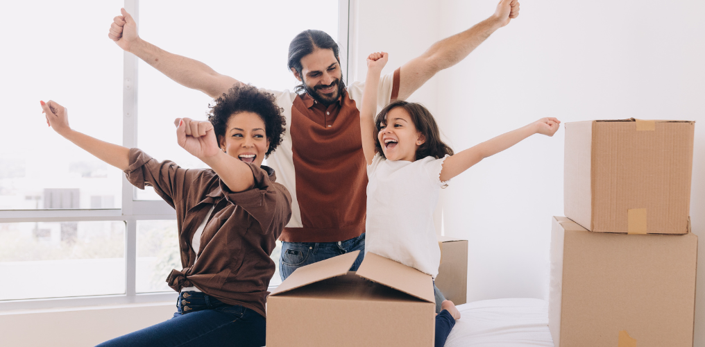 Family sitting on floor, smiling, and packing boxes. 