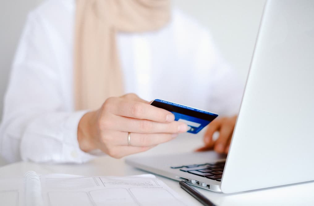 Hand holding debit card near laptop.