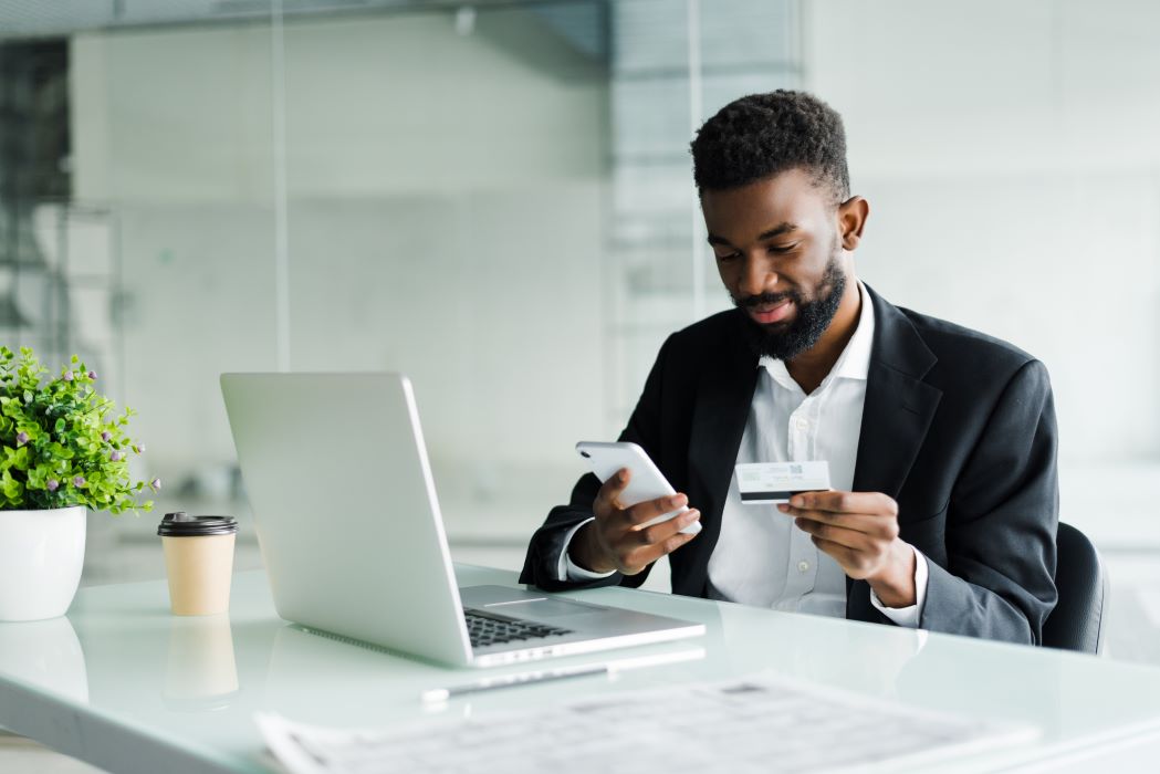 Man looking at phone at desk and using debit card.