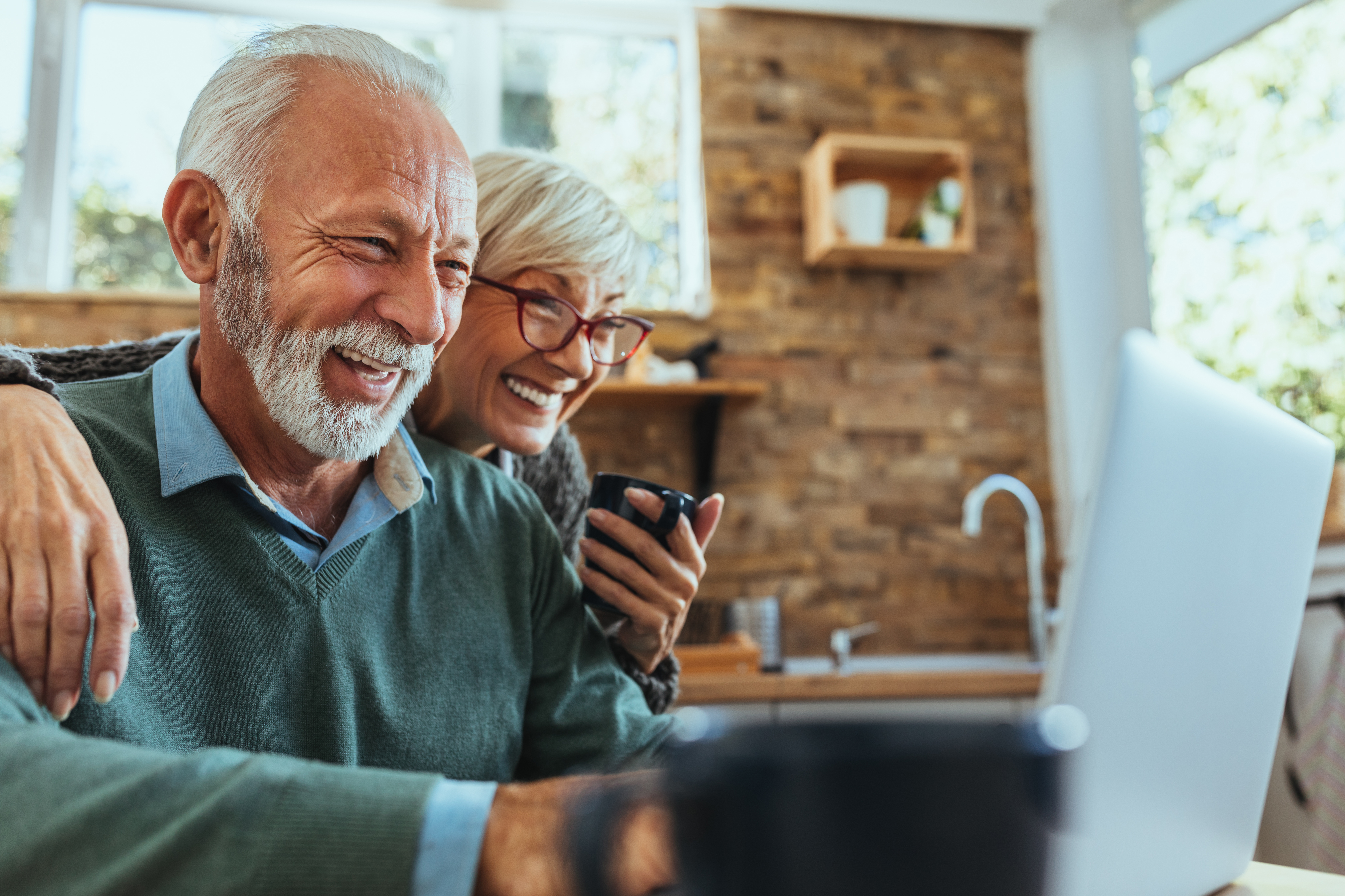 elderly couple laughing in front of laptop.