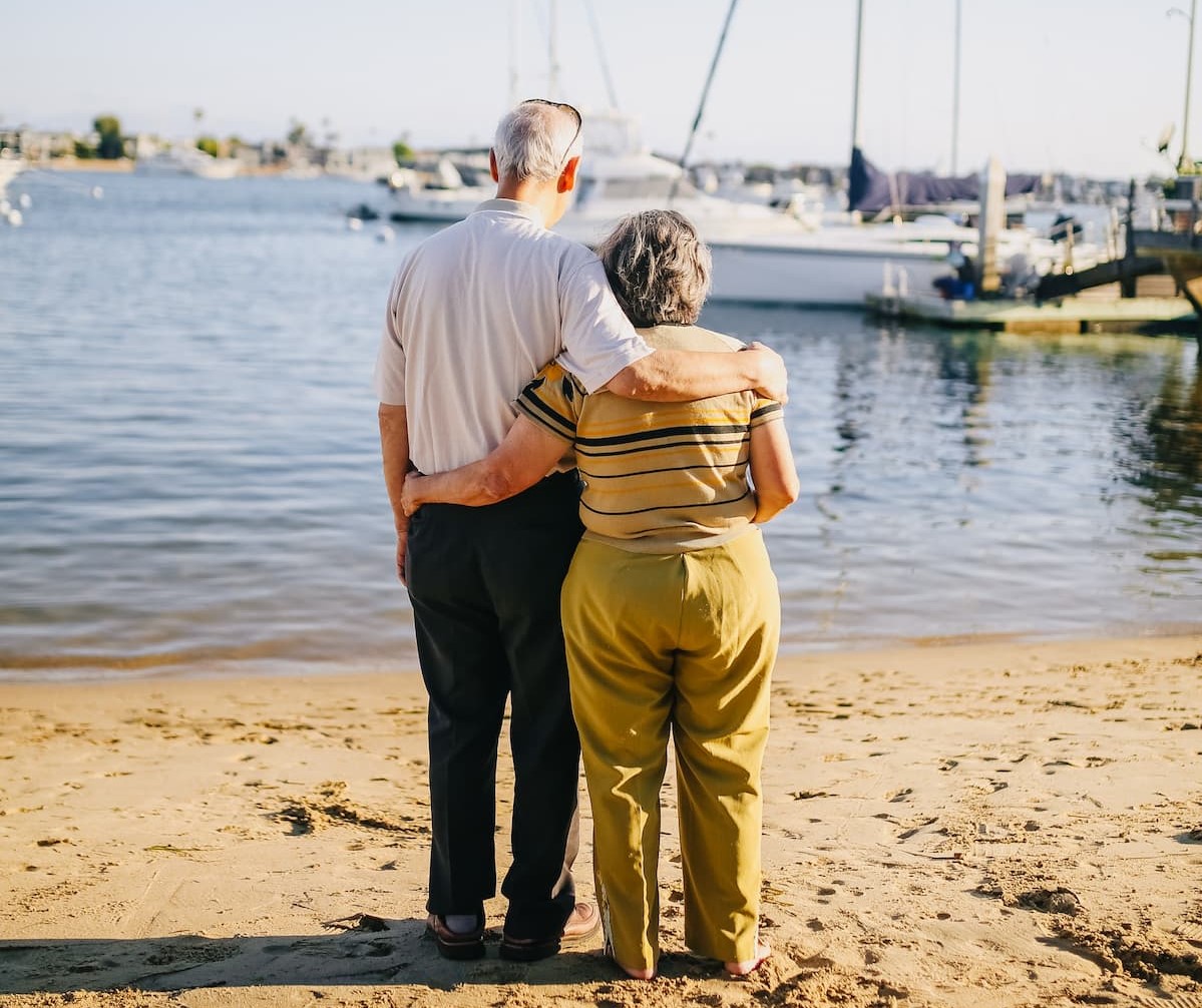 elderly couple looking out from beach to boats. 