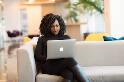 Woman with Apple laptop sitting on nice couch in modern home or office.