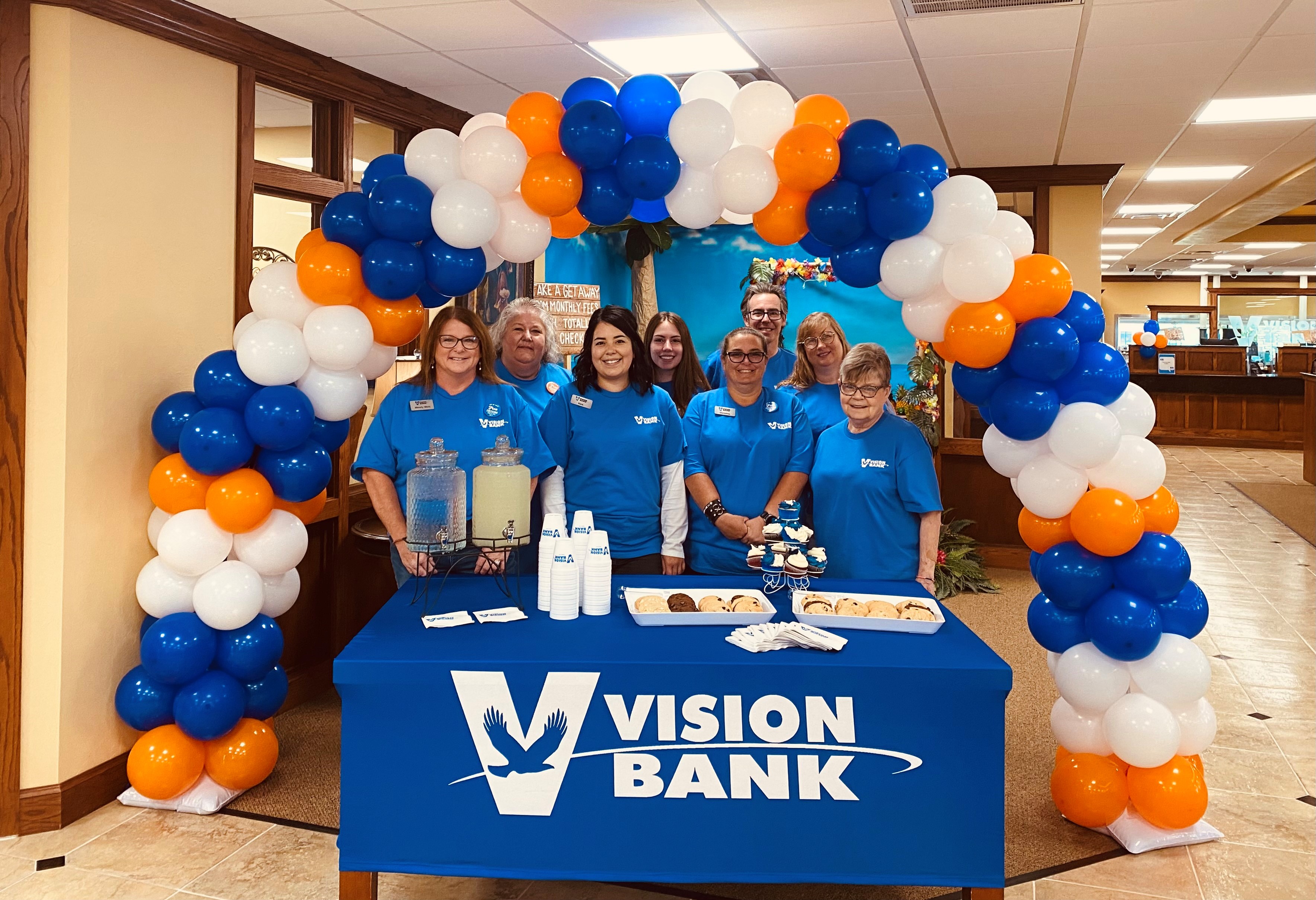 Vision Bank employees in front of balloon arch. Table with cookies and giveaways.