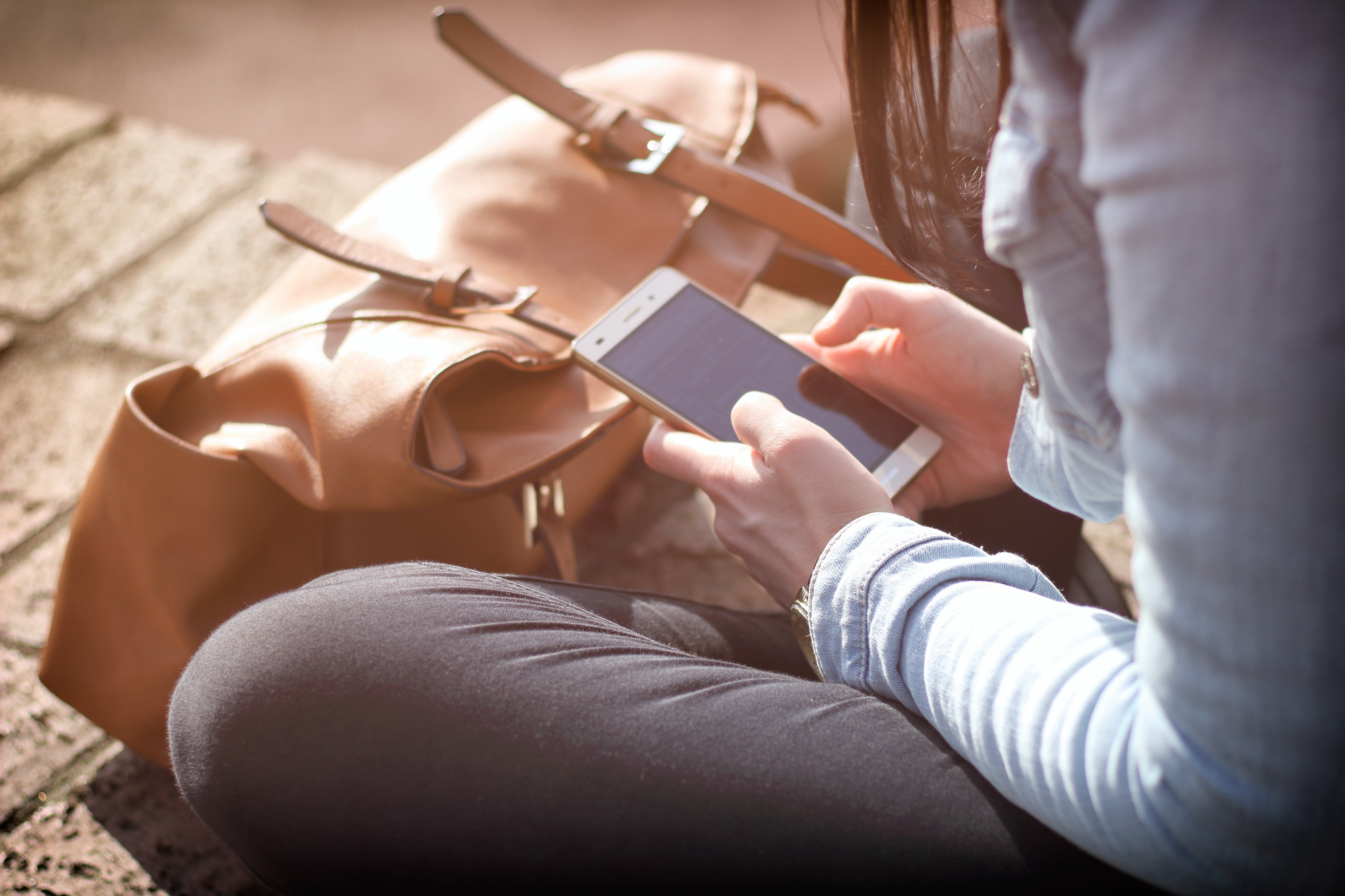 Person sitting on brick walkway looking at smartphone.