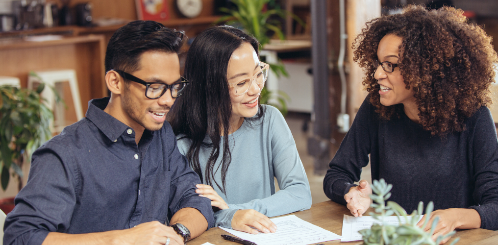 Three people sitting at table going over papers. 