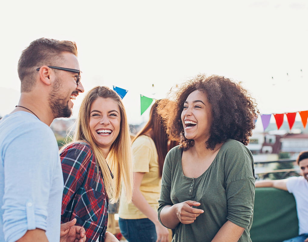 Three friends laughing outside at party.