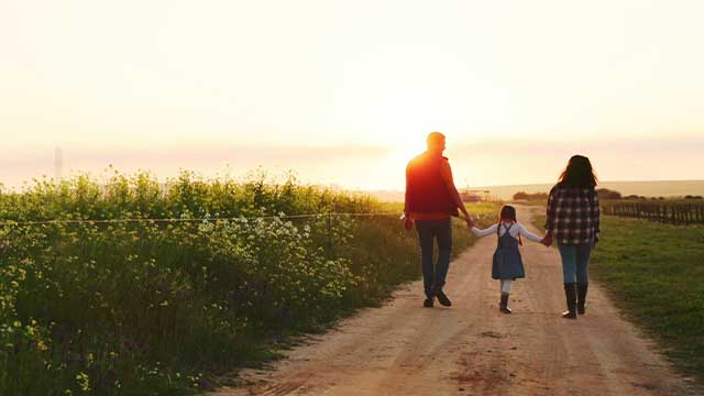 Family walking on dirt path on land with sunset in background