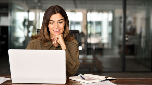 woman sitting at table smiling at laptop computer working