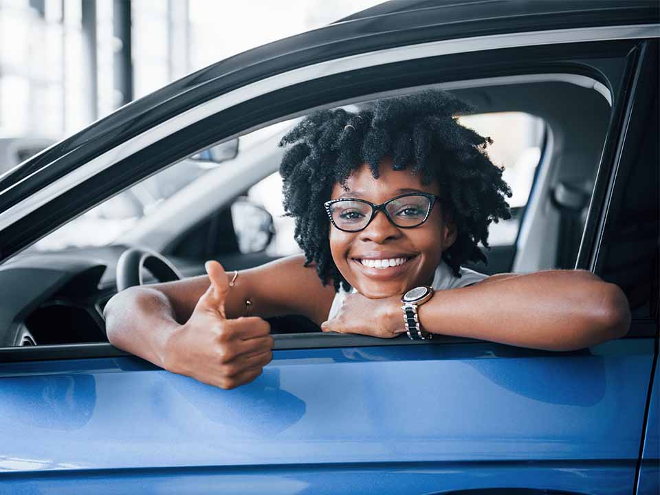 Girl giving a thumbs up smiling out window of car. 