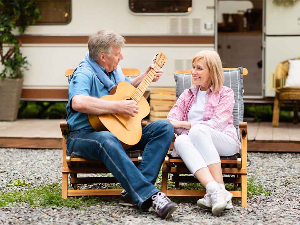 couple sitting outside rv with husband playing guitar