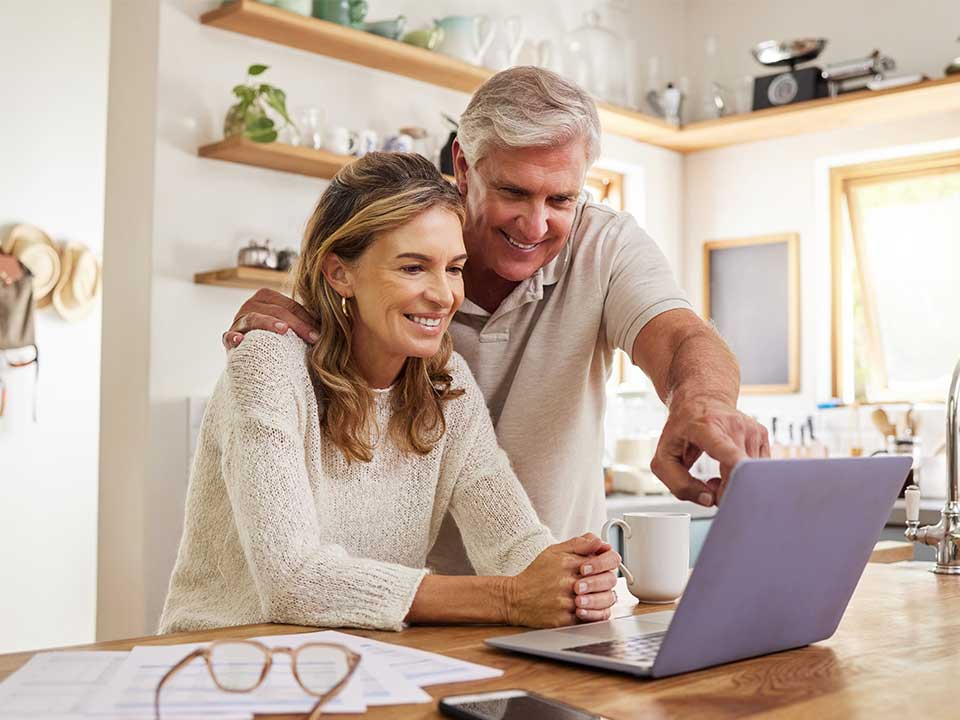 Couple smiling looking at computer in kitchen